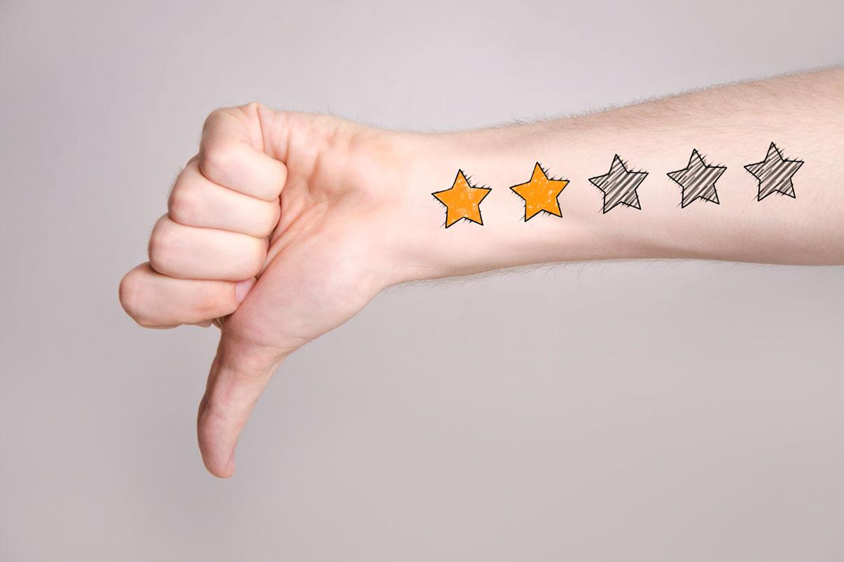 Hand pointing thumbs-down with tattoo of a two-star review on the forearm